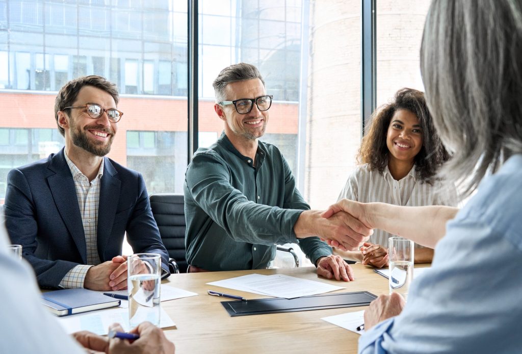 Happy businessman and businesswoman shaking hands at group meeting.
